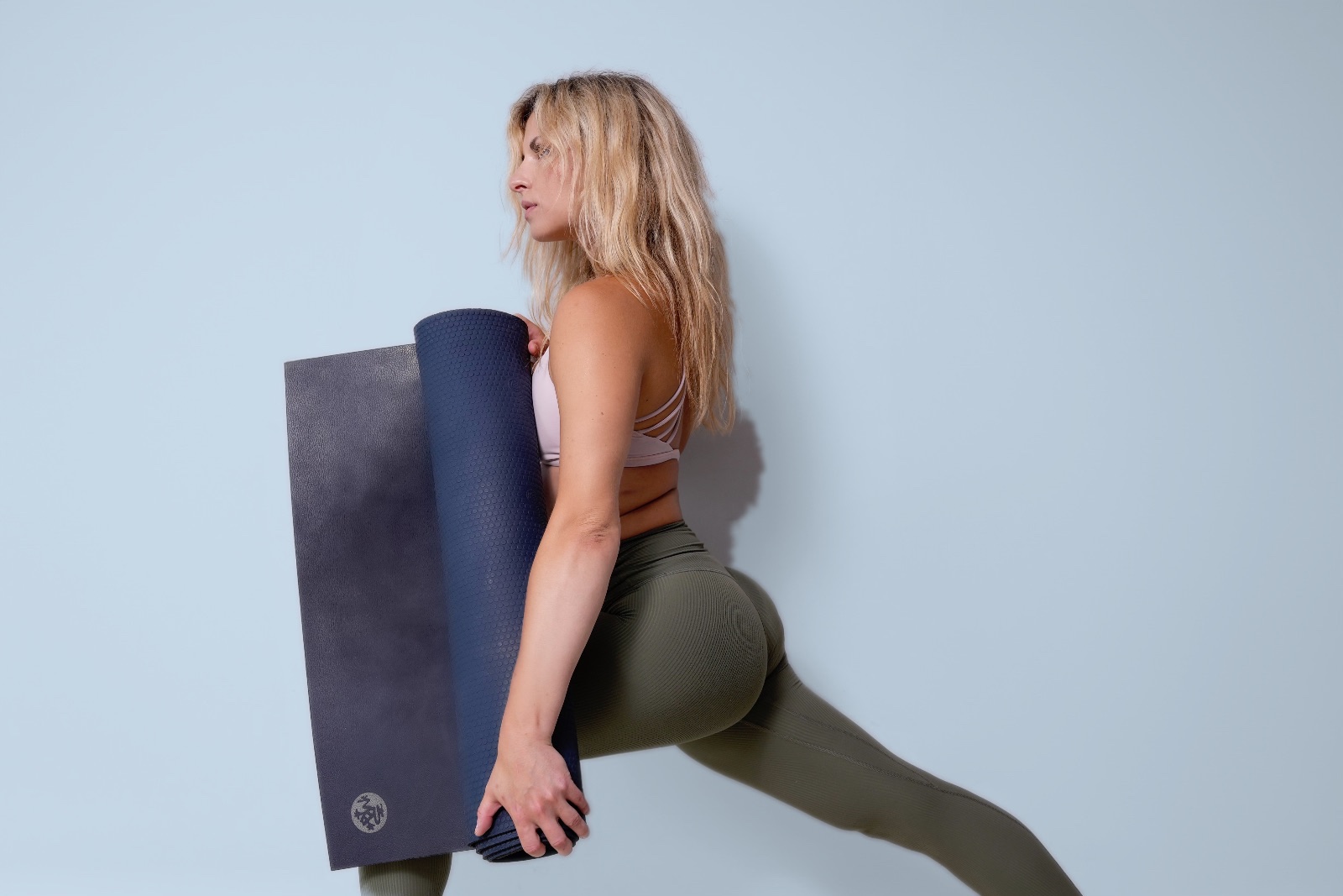 A Yogi in a low lunge holding a rolled yoga mat