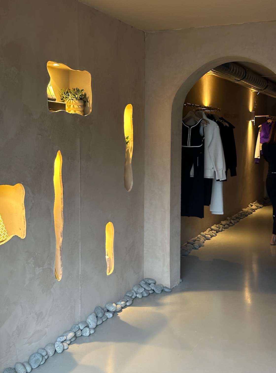The plastered YOGI hallway with lit wall niches and an arch to the boutique