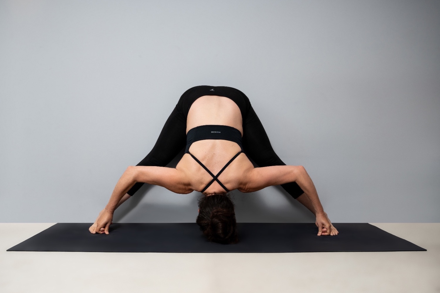 A Yogi in a wide-legged forward fold on a Manduka mat